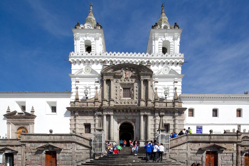 A grand cathedral with two bell towers, a large arched entrance, and a crowd of people at the base.