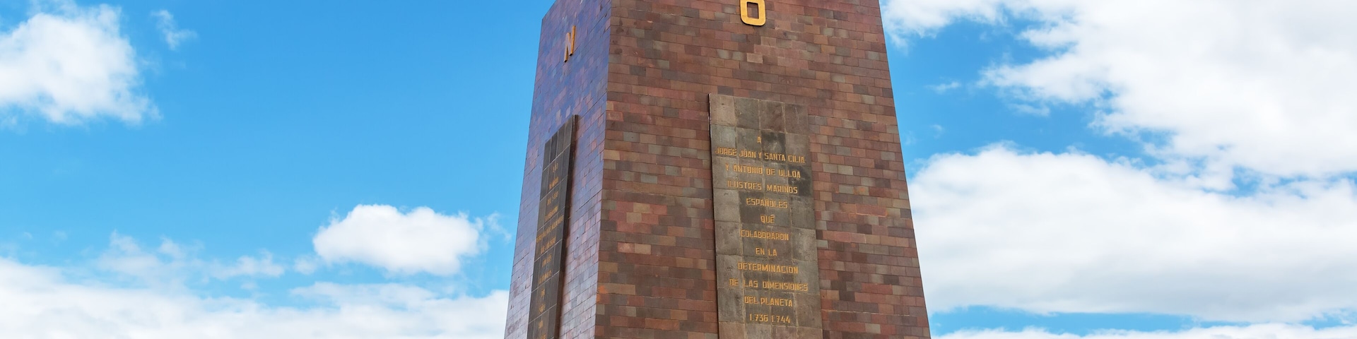Un monumento de ladrillo con un globo terráqueo en la parte superior, banderas y una placa.