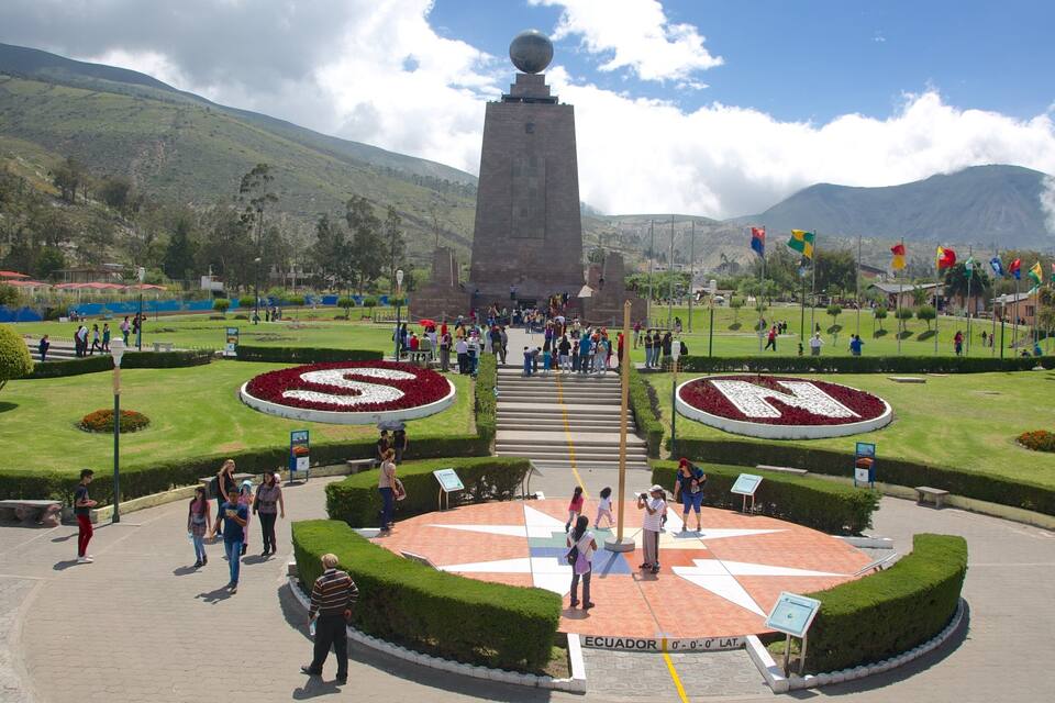 Un monumento con una parte superior esférica, rodeado por un jardín circular con un diseño en forma de estrella, y un paisaje montañoso de fondo.