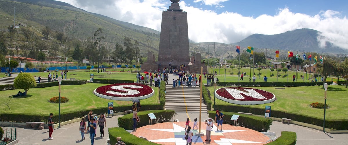 A monument with a spherical top, surrounded by a circular garden with a star-shaped design, and a mountainous backdrop.