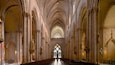A cathedral interior with high vaulted ceilings, rows of pews, and stained glass windows.