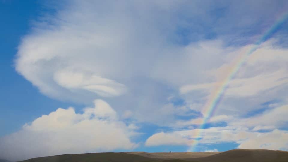 A landscape with rolling hills and a rainbow in the sky.
