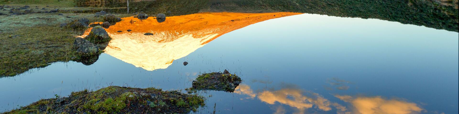 A breathtaking view of the snow-capped Cotopaxi volcano in Ecuador's Parque Nacional Cotopaxi, with Laguna de Santo Domingo in the foreground.