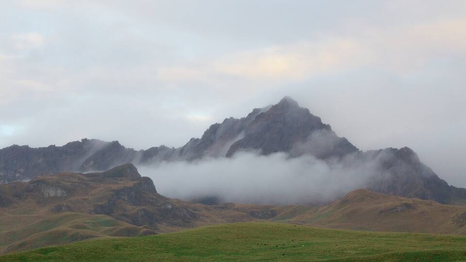 A mountain range with a prominent peak partially obscured by clouds.