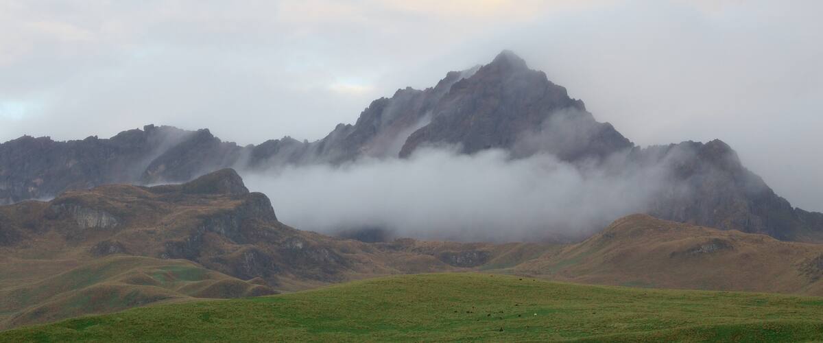 A mountain range with a prominent peak partially obscured by clouds.