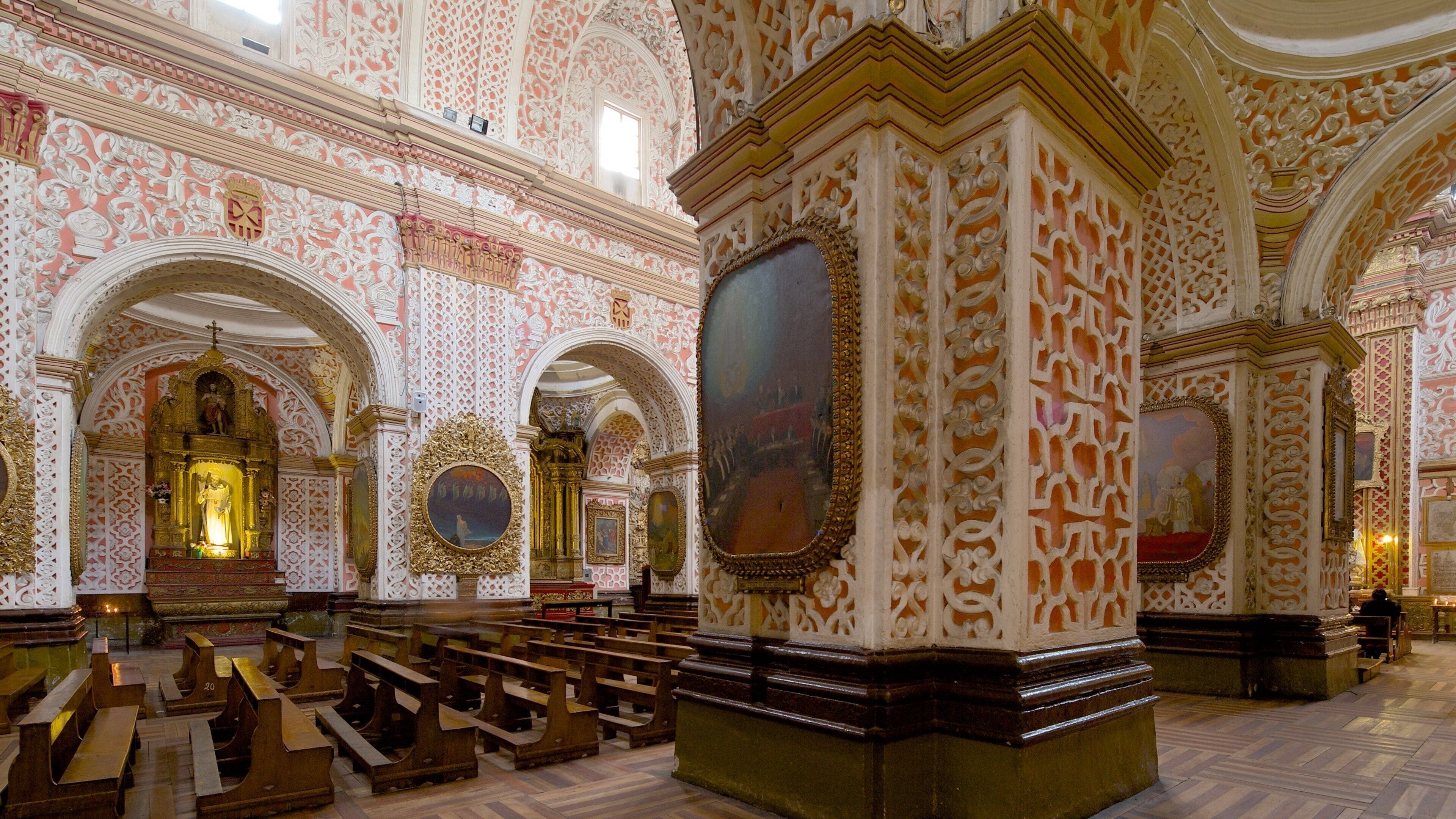 L’intérieur d’une église richement décorée, avec des motifs complexes sur les murs, des bancs en bois et des peintures religieuses.
