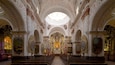 An ornate church interior with intricate ceiling designs, a central altar, and rows of pews.