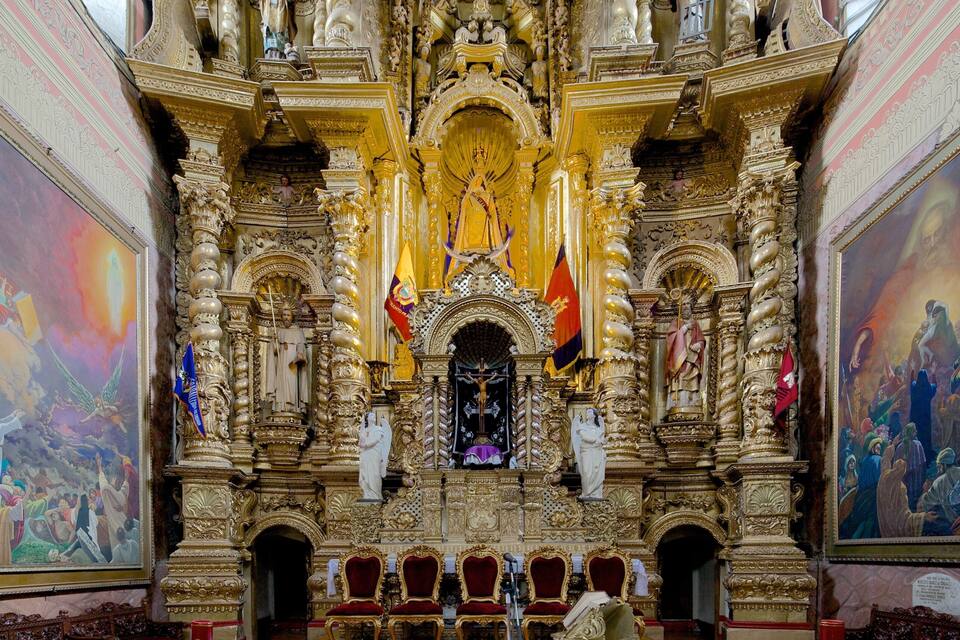 Interior de igreja ornamentado com decorações douradas, um altar central e pinturas religiosas nas paredes.