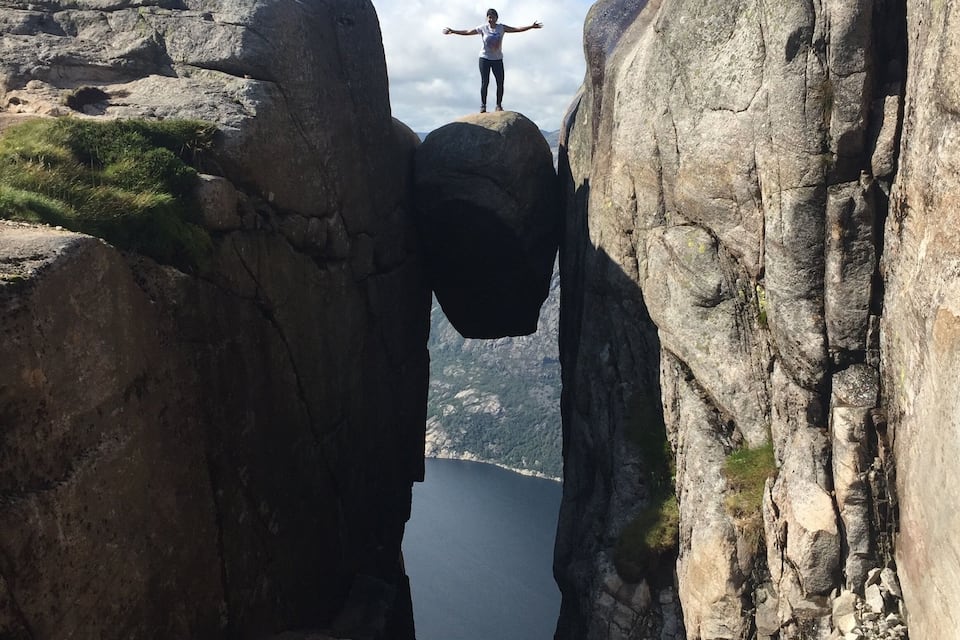 Uma pessoa em uma saliência rochosa entre duas formações rochosas, com um lago ao fundo.