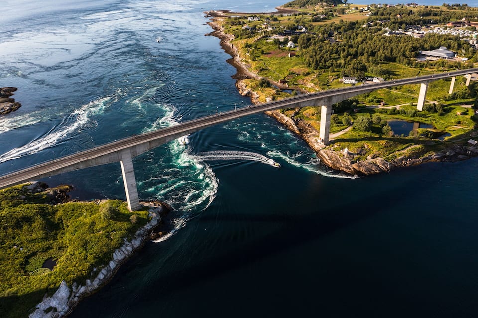 A bridge spanning a fjord with a coastal village and greenery.