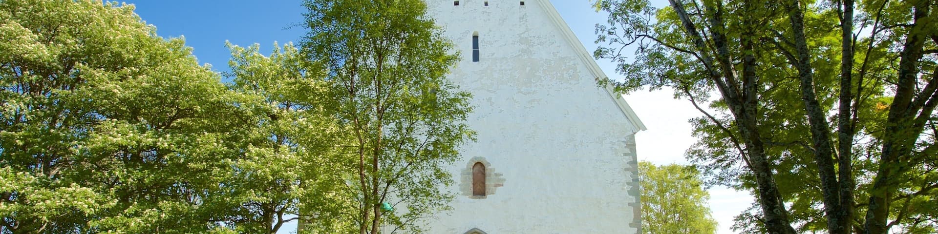 A white church with a pointed roof, surrounded by trees and a cemetery.