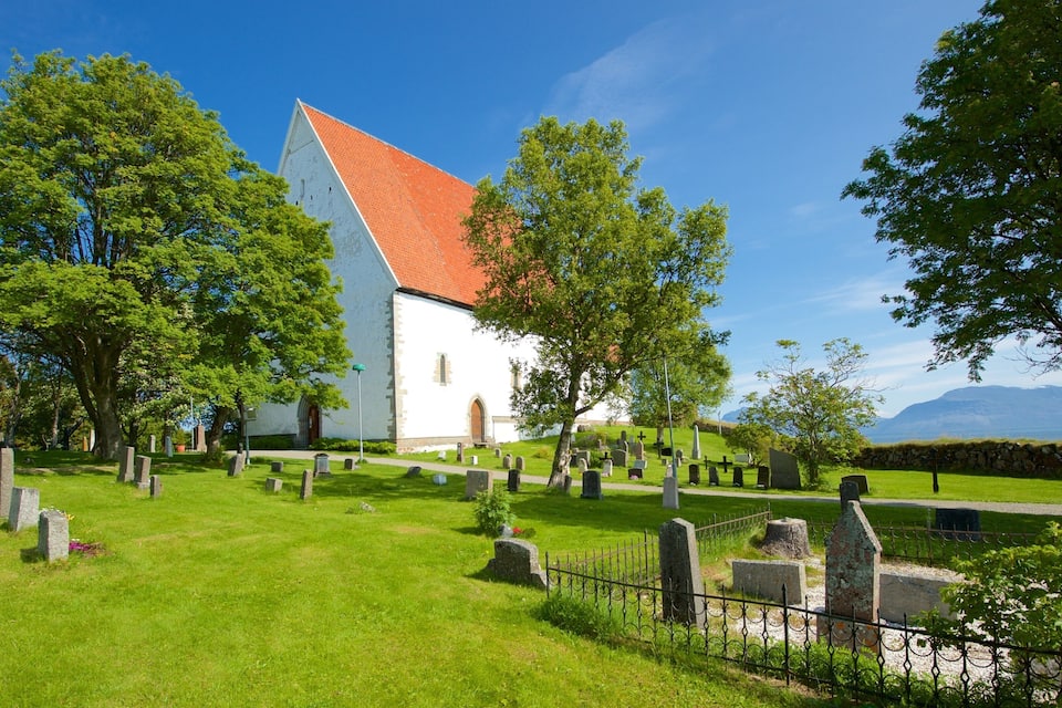 En kirke med rødt tag, omgivet af en kirkegård med gravsten og træer.