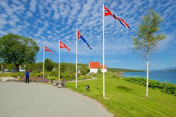 A coastal road with flags, a white house, and a lake.