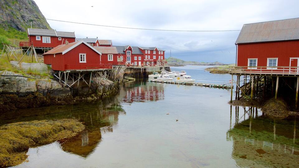A coastal village with red buildings on stilts over water, a dock with boats, and a mountainous backdrop.