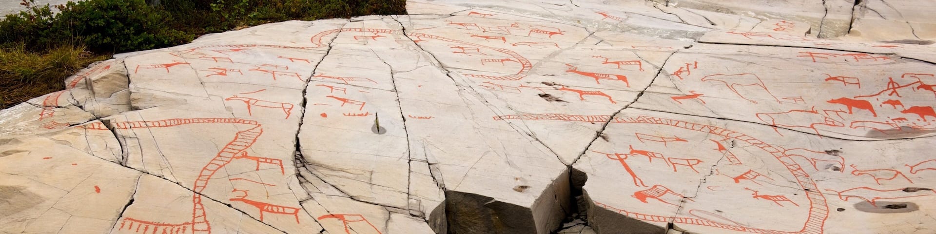 Ancient rock art with red drawings of animals and symbols on a large rock surface.