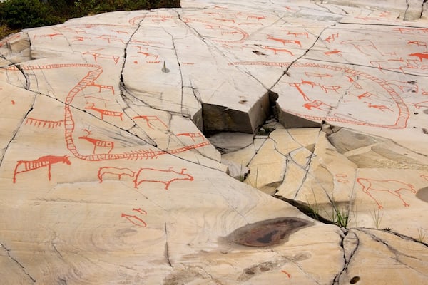 Ancient rock art with red drawings of animals and symbols on a large rock surface.