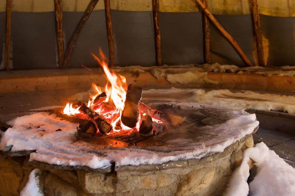 Un foc a terra de pedra amb llenya encès en un ambient rústic.