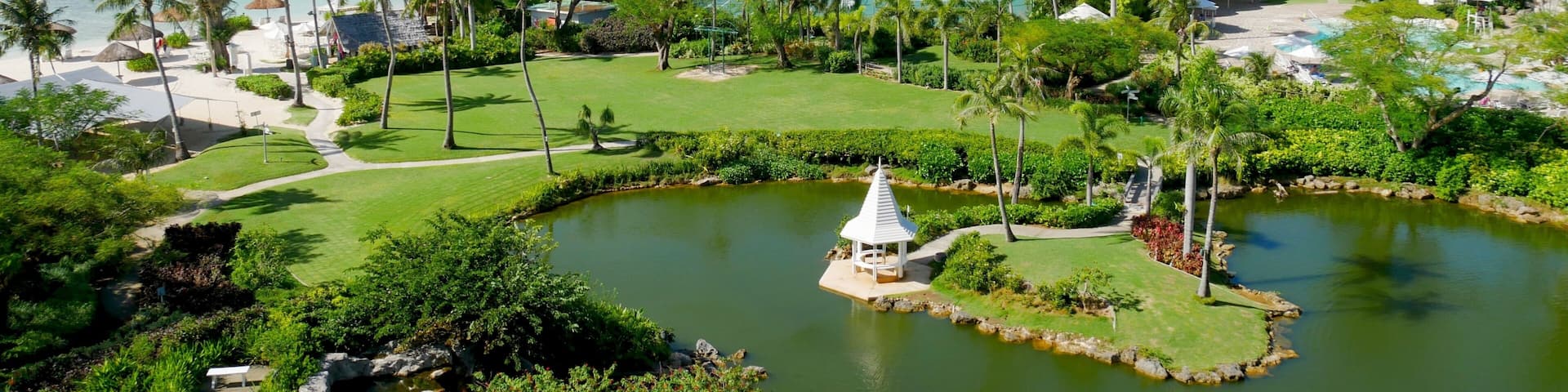 Landscaped gardens Pristine blue waters of the Micro Beach and the far-off Managaha Island backdrops a perfectly manicured garden with pond in Saipan, Northern Mariana Islands.