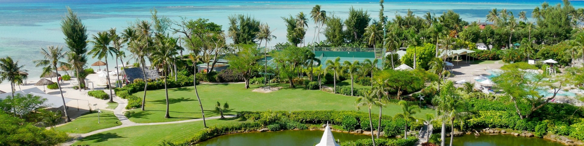 A tropical resort with a golf course, a pond with a gazebo, and a beach with palm trees.