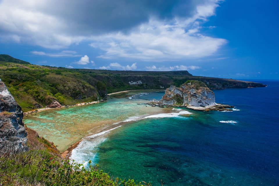 Paisagem costeira com águas turquesa cristalinas, falésias rochosas e vegetação exuberante.