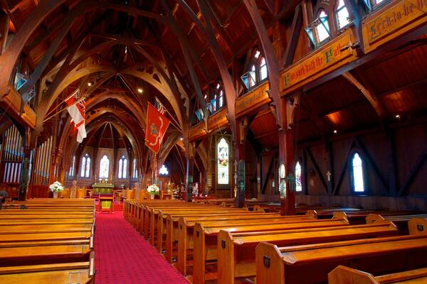 A church interior with wooden pews, a red carpet, and stained glass windows.