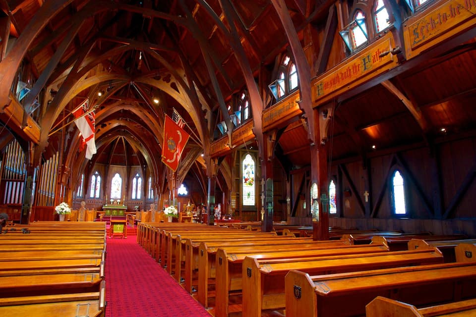 Een kerkinterieur met houten banken, een rood tapijt en glas-in-loodramen.
