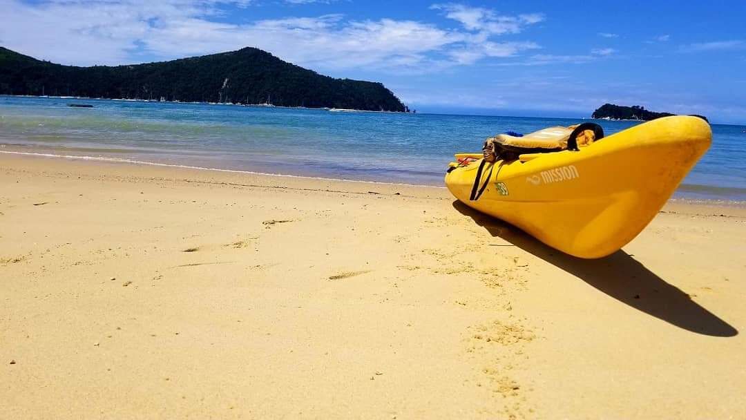 Una lancha inflable amarilla en una playa arenosa con un mar azul cristalino y una isla boscosa al fondo.