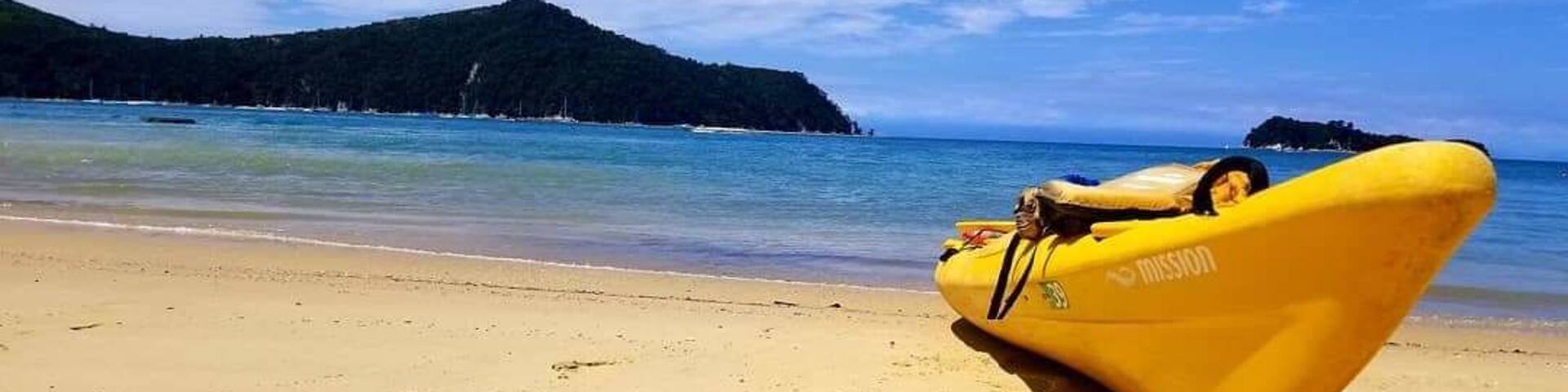A yellow inflatable boat on a sandy beach with a clear blue sea and a forested island in the background.