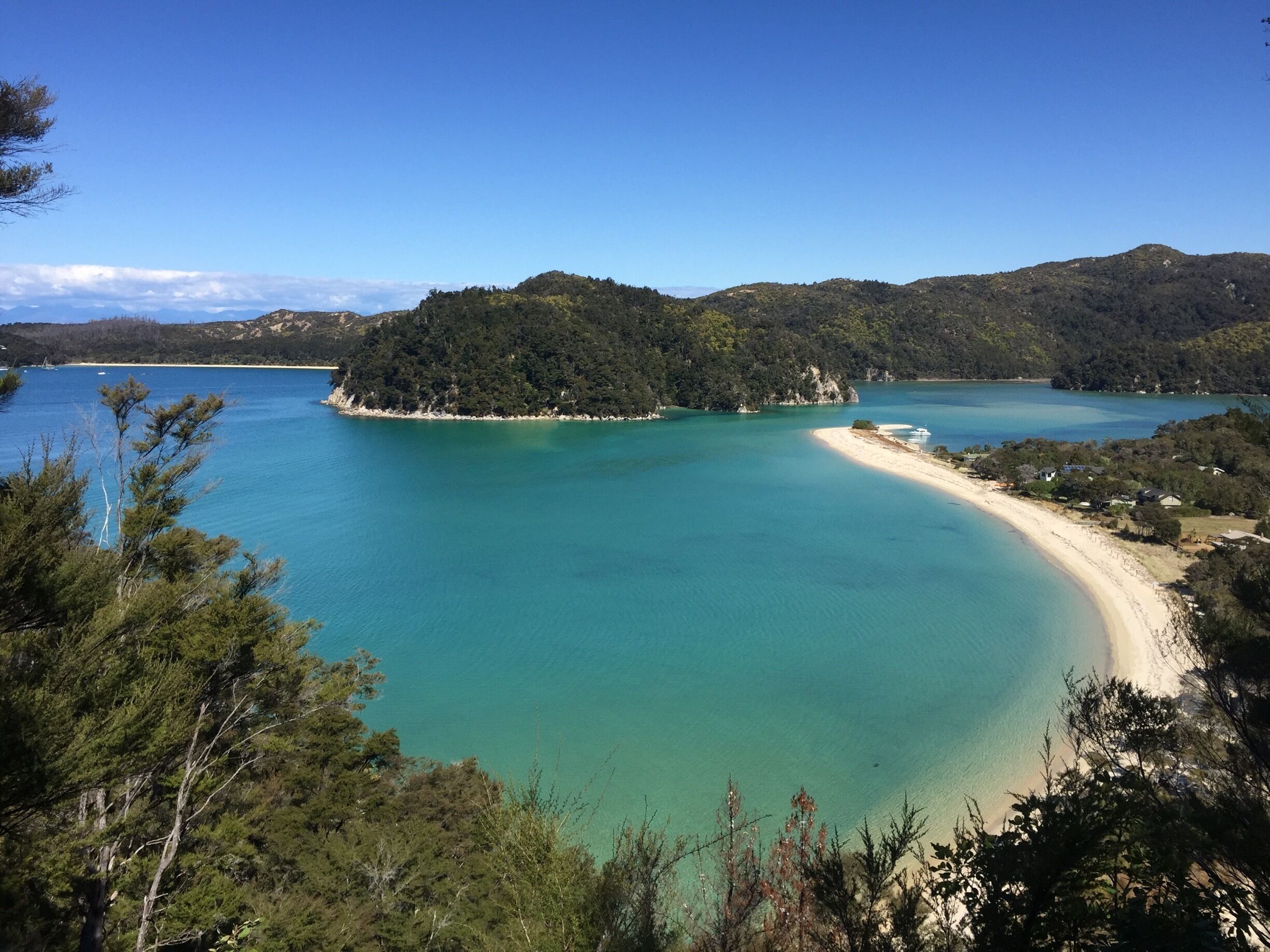A turquoise bay with a sandy beach, surrounded by dense forest and hills.