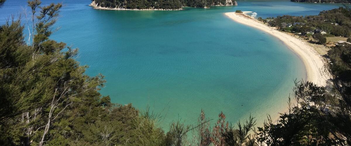 A turquoise bay with a sandy beach, surrounded by dense forest and hills.