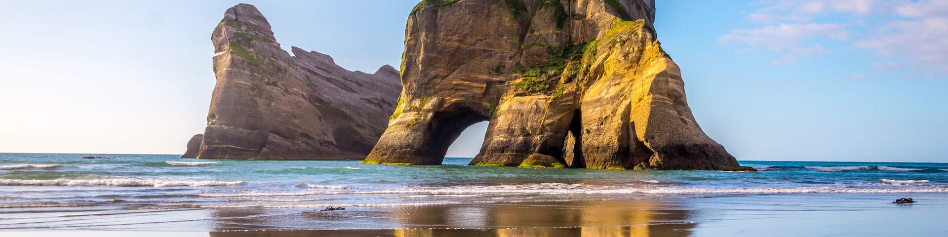 A coastal rock formation with a natural arch, a sandy beach, and the ocean.