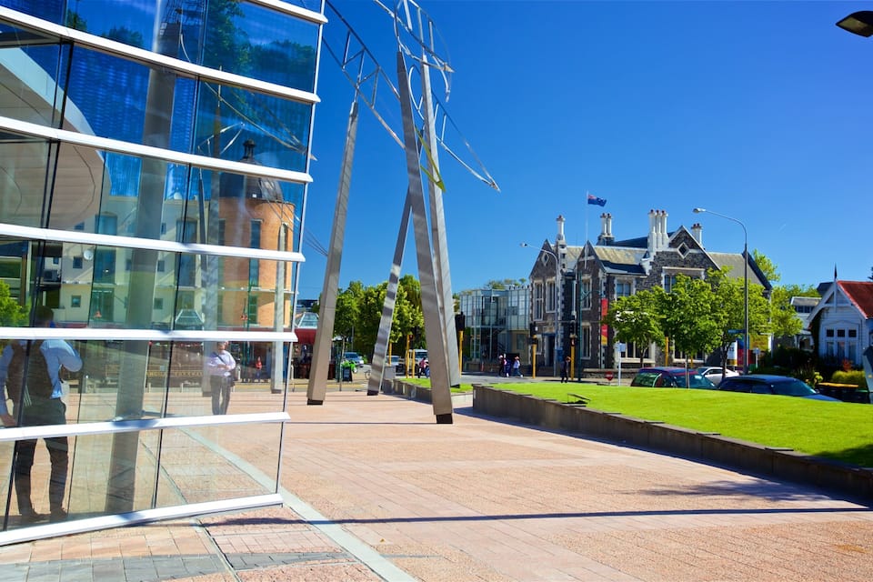 A modern glass building, a street with cars, and traditional houses.