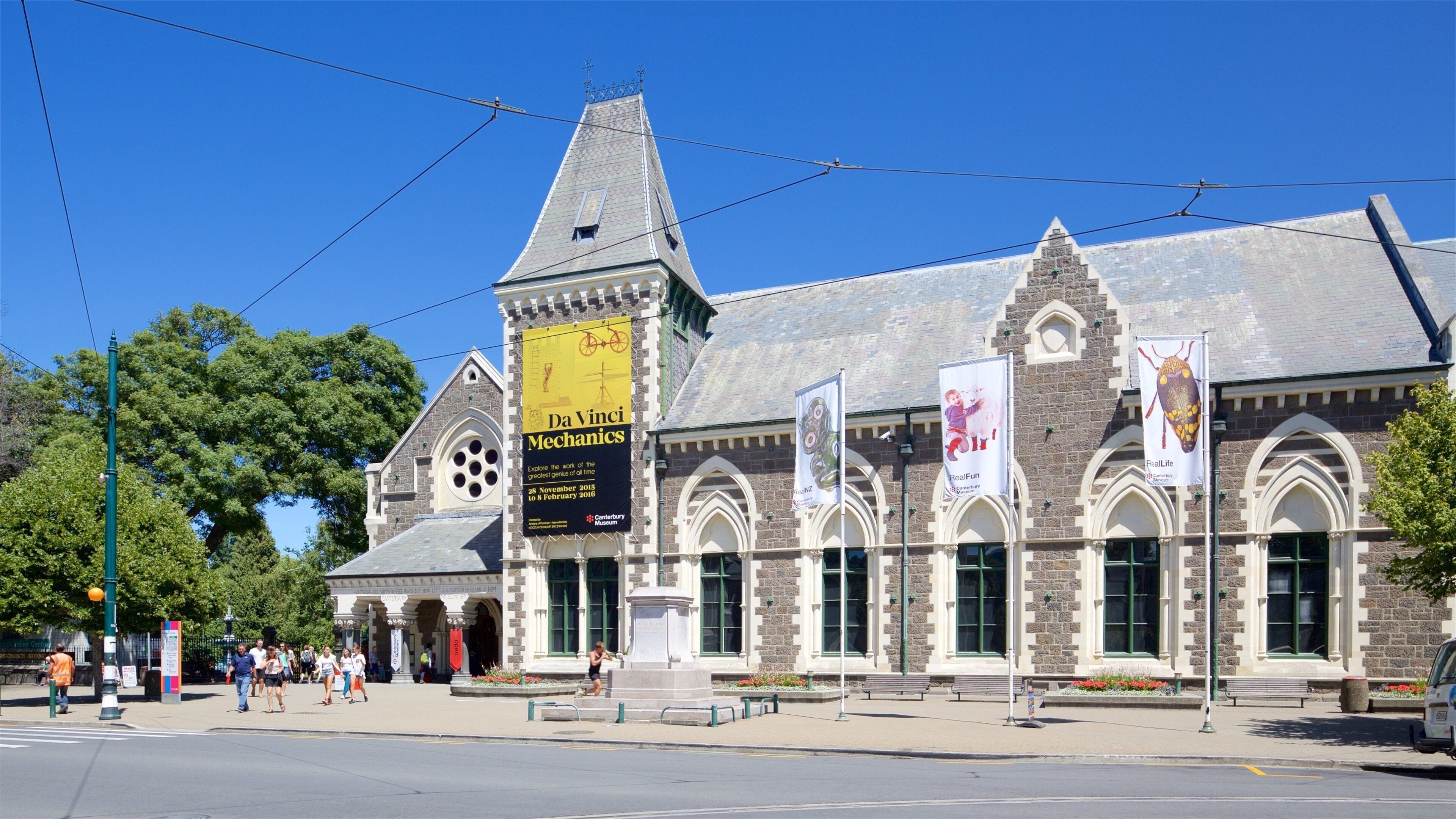 A historic building with a clock tower, banners, and a statue in front.