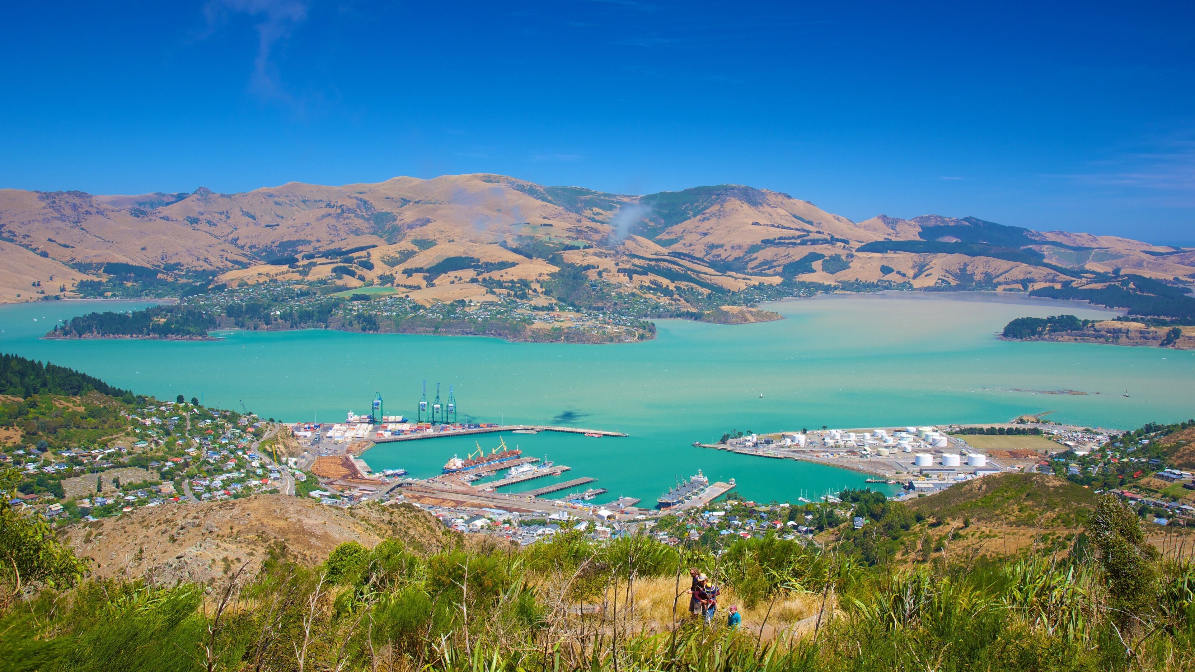 A coastal town with a harbor, mountains in the background, and a clear blue sky.