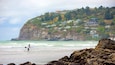 Una spiaggia con onde, un surfista e case su una collina.