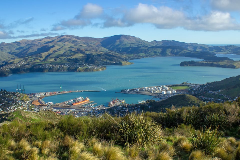 A coastal town with a harbor, mountains in the background, and a clear sky.