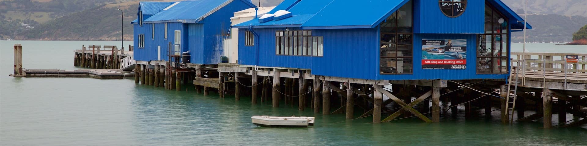 A blue pier with buildings, a boat, and mountains in the background.