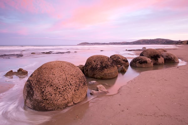 Moeraki Boulders showing a sandy beach, rugged coastline and a sunset