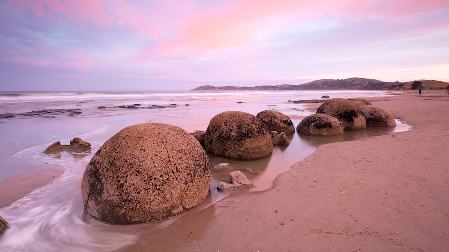 Moeraki Boulders ofreciendo una puesta de sol, costa escarpada y una playa