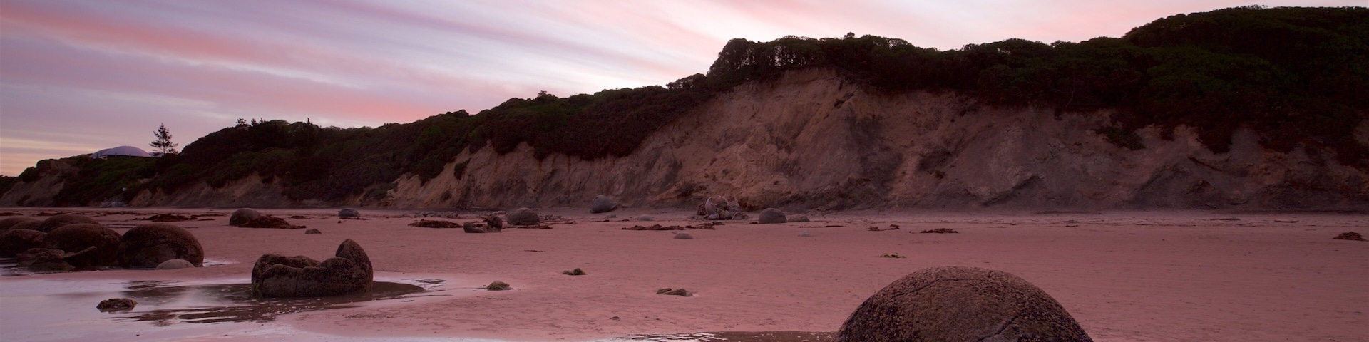 Moeraki Boulders welches beinhaltet Sonnenuntergang, schroffe Küste und Strand