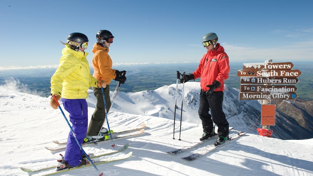 Skifahrer auf einem verschneiten Berg, ein Wegweiser zeigt die Richtung zu verschiedenen Skipisten.