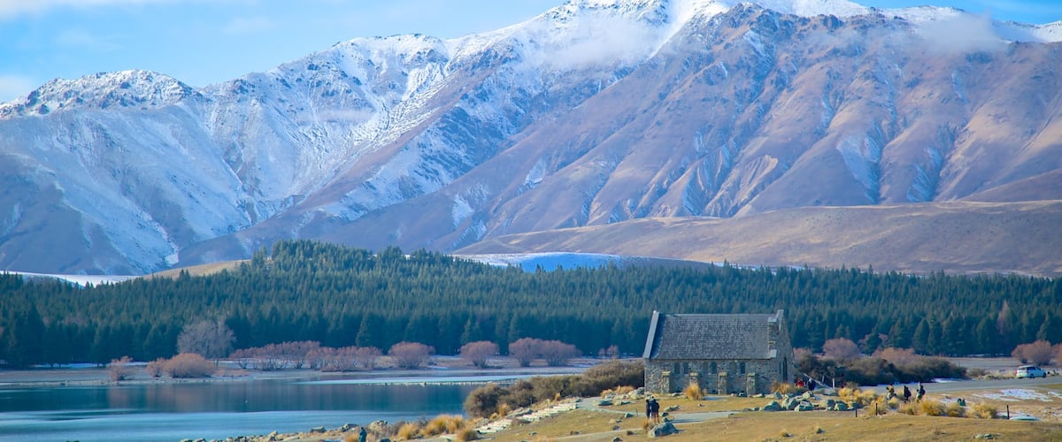 A mountain range with a lake and a stone building in the foreground.