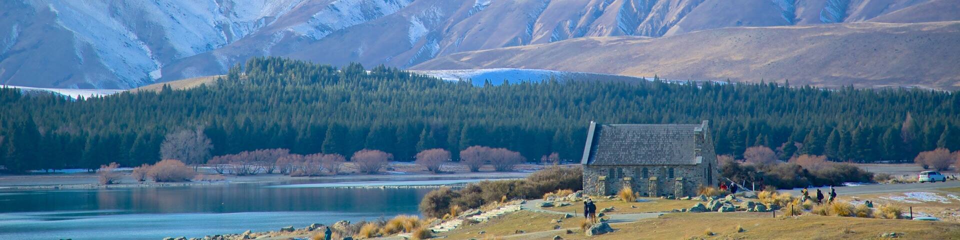 A mountain range with a lake and a stone building in the foreground.