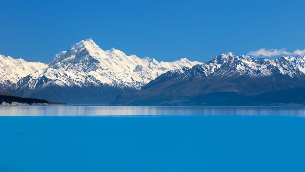 Une chaîne de montagnes aux sommets enneigés, avec un lac bleu et paisible au premier plan.