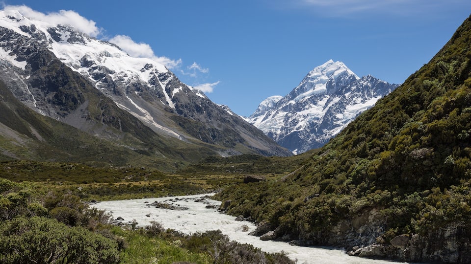 A river flowing through a valley with snow-capped mountains in the background.