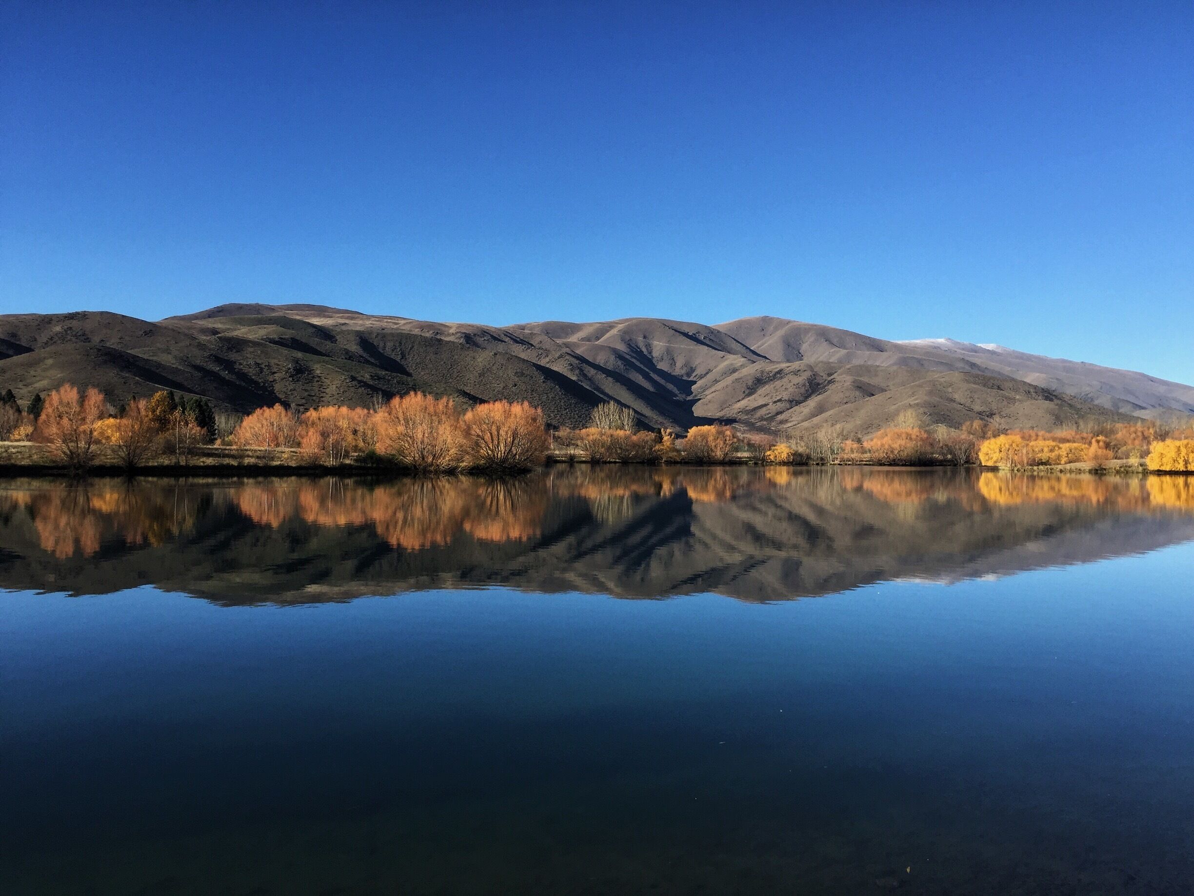 A calm lake reflecting mountains and autumn-colored trees.