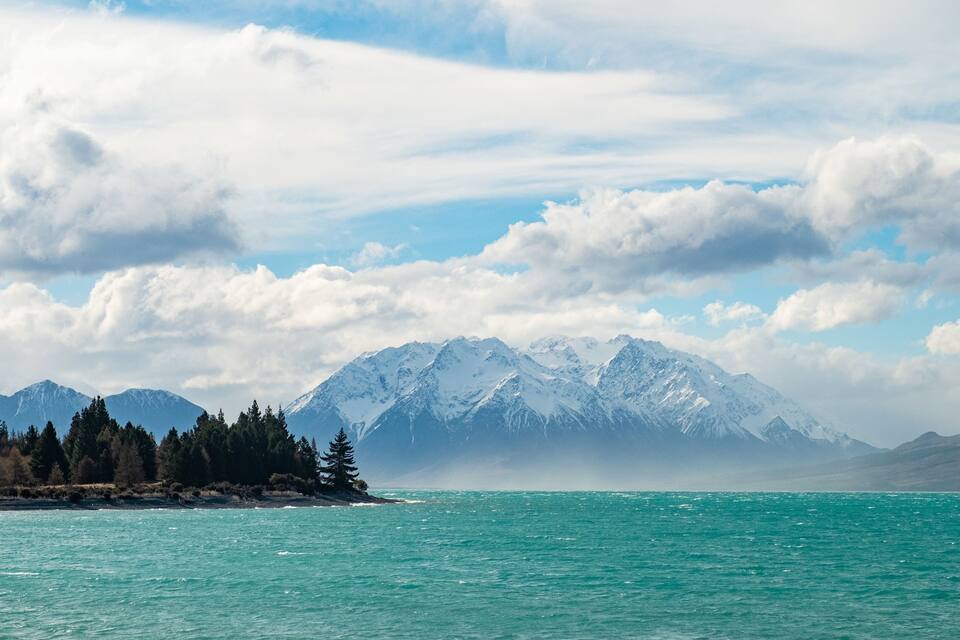 A turquoise lake with snow-capped mountains in the background and a forested shoreline.