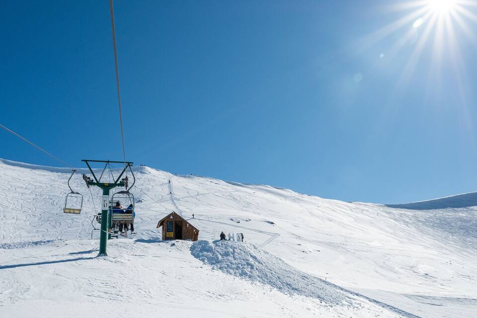 A ski lift on a snowy mountain with a clear blue sky.