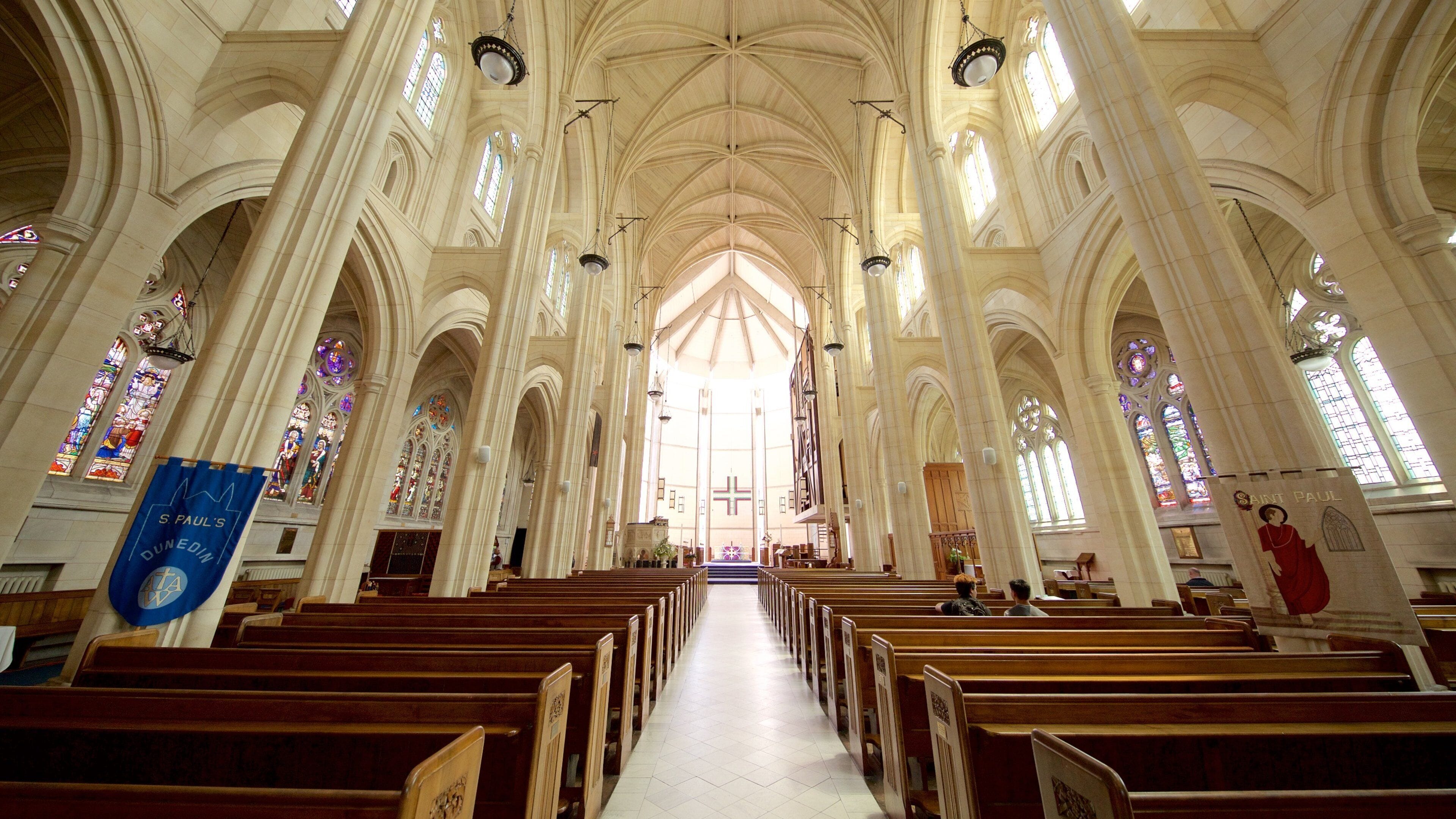 L’intérieur d’une cathédrale, avec de hauts plafonds en voûte, des vitraux et des rangées de bancs.