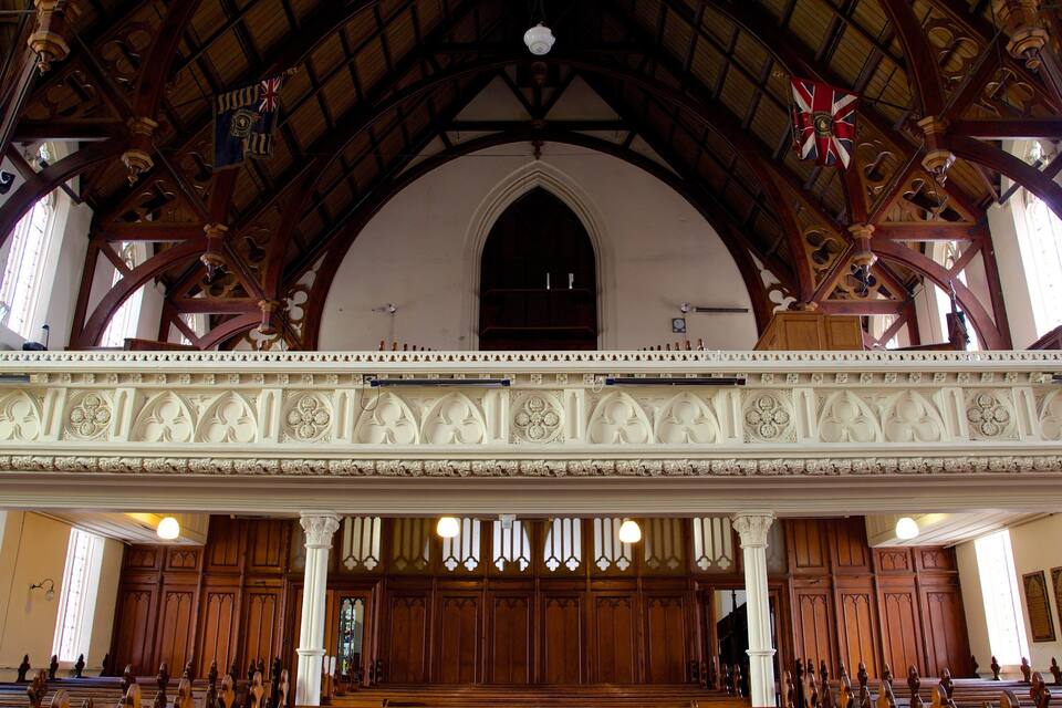 An ornate church interior with wooden beams, a balcony, and stained glass windows.